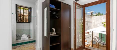 A compact bathroom with a shower, a built-in wardrobe, and a small window with a view of the outside.