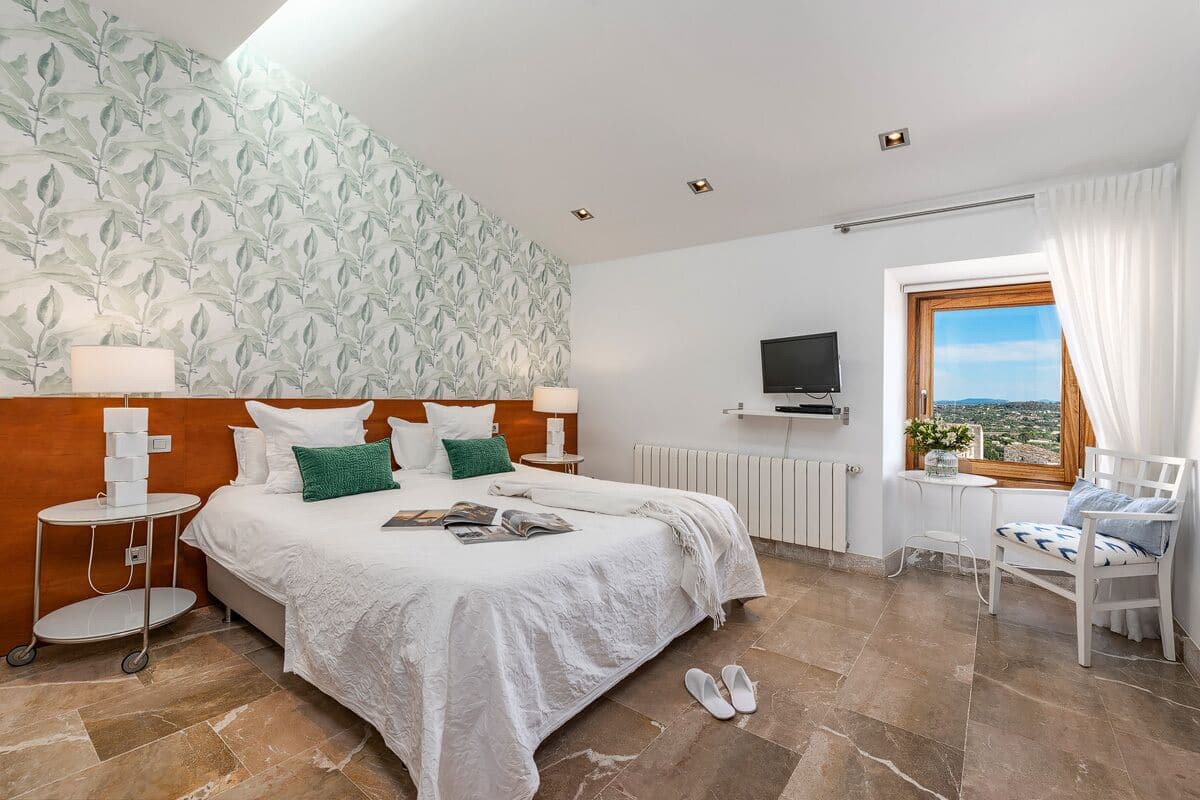 A bedroom with a bed, a TV, a window with a view, and a chair.