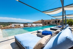 Piscina infinita no terraço com espreguiçadeiras e vista para a paisagem.