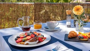 A table set with breakfast, including a plate of fruit, a pitcher of juice, and croissants, with a scenic view in the background. -  Finca Son Arnau (Selva)