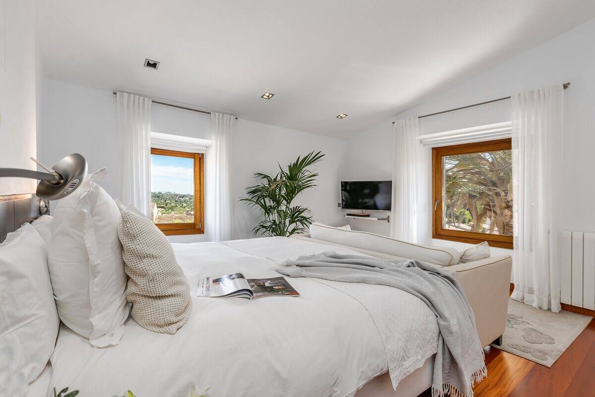 A modern bedroom with a large bed, a TV, and a view of the outdoors.