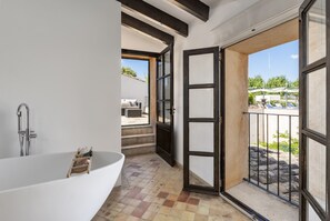 Um banheiro moderno com uma banheira independente, piso revestido e vista para o exterior por uma porta de vidro.