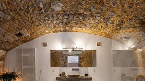 A bathroom with a stone ceiling, a large mirror, a sink, and a towel on the floor. -  Finca Son Arnau (Selva)