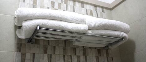 A bathroom with a tiled floor, a towel rack with folded towels, and a ceiling with a skylight.