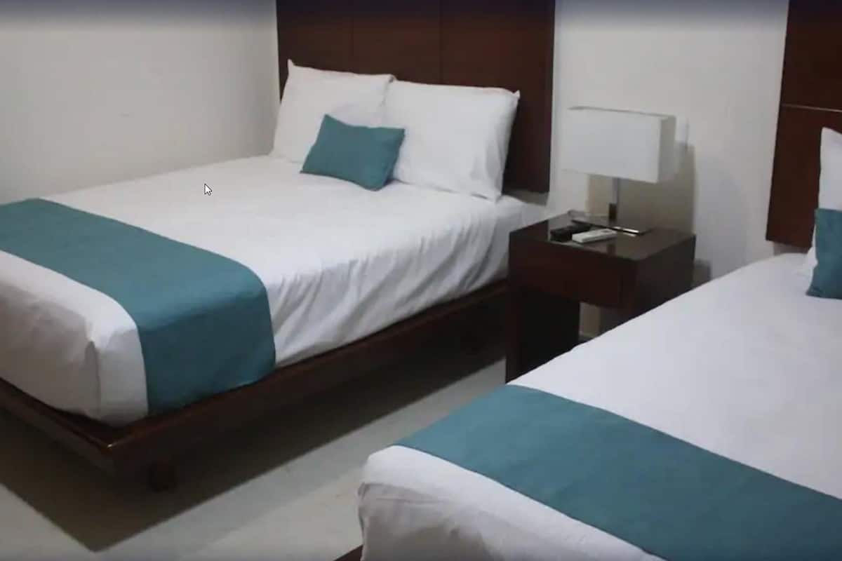 Two single beds with white and teal bedding, a nightstand with a lamp, and a wooden headboard.