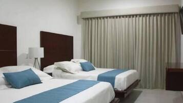 Habitación de hotel con dos camas, un escritorio, una lámpara y un televisor.