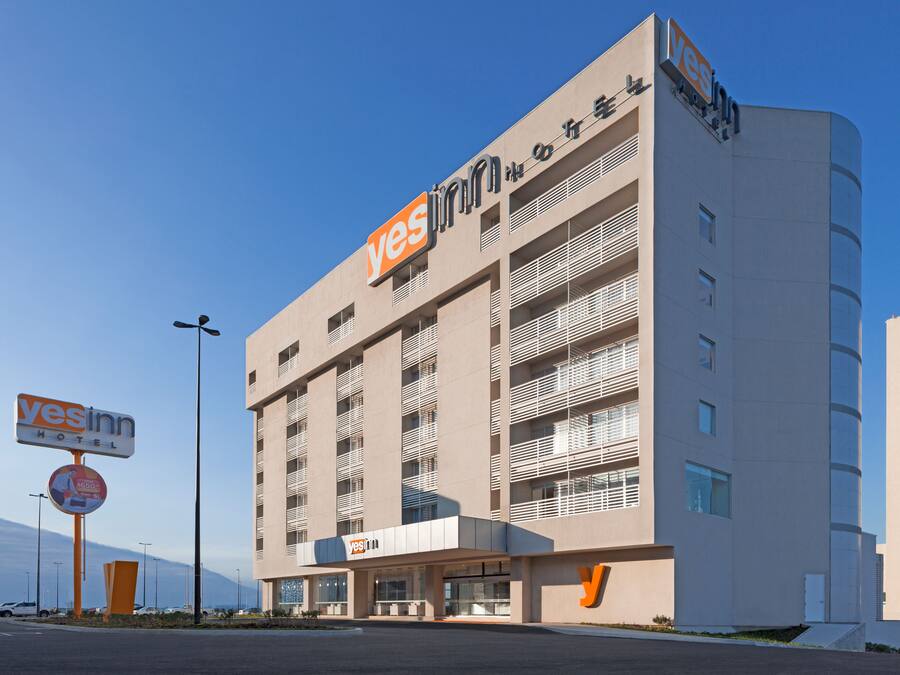 Een modern hotelgebouw met een opvallend ‘yesinn’ bord, meerdere balkons en een heldere lucht.