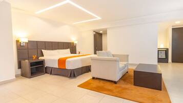 A modern hotel room with a large bed, a sofa, a nightstand, and a small table.