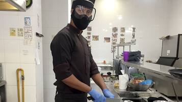 Un chef en una cocina con paredes de azulejos blancos, mostradores de acero inoxidable y diversos utensilios de cocina.
