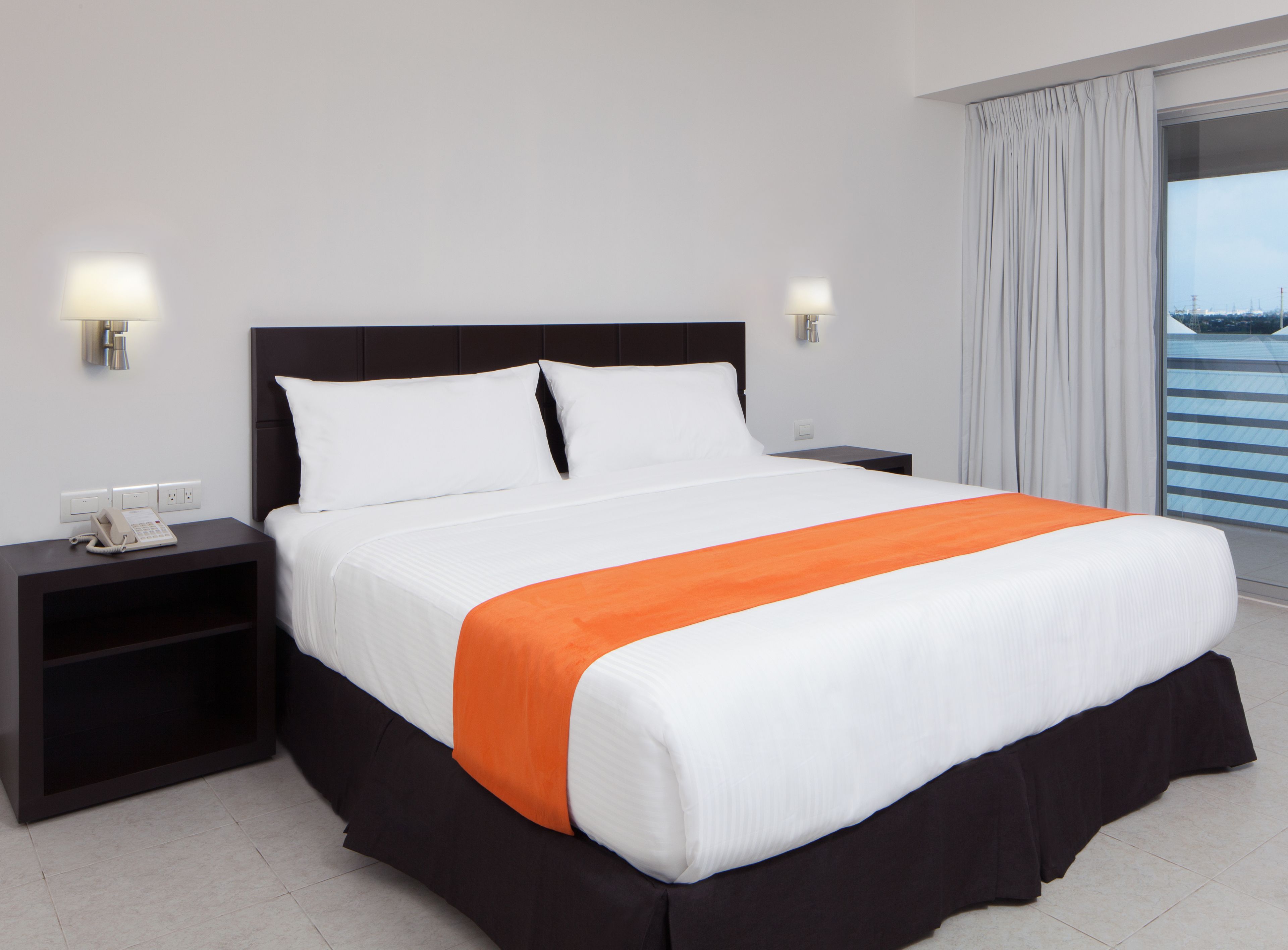A hotel room with a bed, nightstands, a telephone, and a view of the outside.