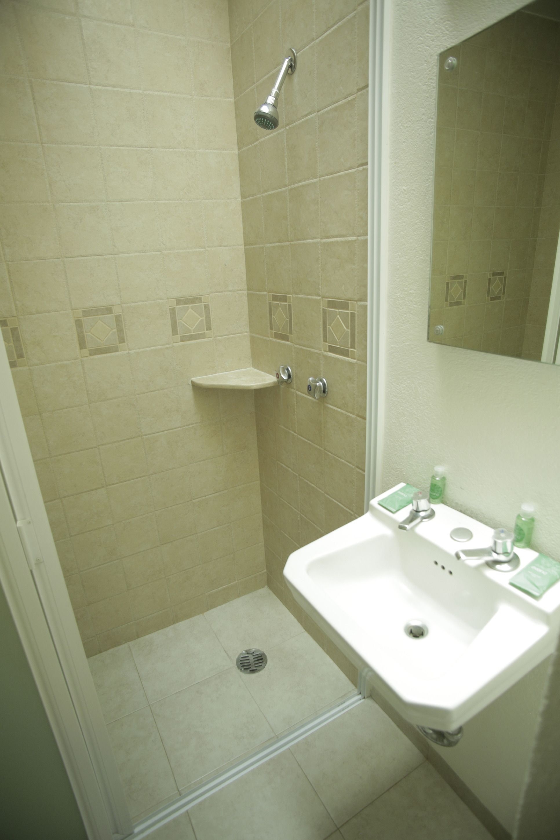 A bathroom with beige tiles, a shower, a sink with a mirror, and toiletries.