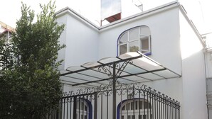 A white building with a balcony, a blue door, and a potted plant with pink flowers. - Hotel Casa González (Mexico City)