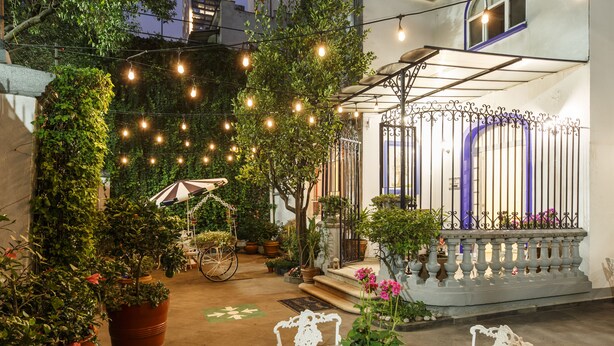 An outdoor patio area with string lights, potted plants, a bicycle, and a white chair. - Hotel Casa González (Mexico City)