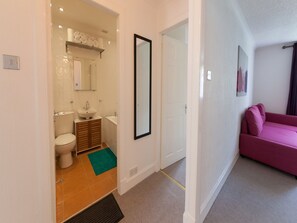 A modern bathroom with a toilet, sink, and mirror. There is a green mat on the floor and a pink sofa in the adjacent room. - Leith Apartments (Edinburgh)