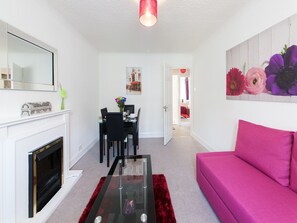A living room with a fireplace, a dining area, and a vibrant pink sofa. - Leith Apartments (Edinburgh)