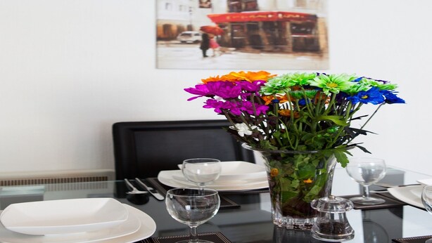 Et spisebord dækket med tallerkener, bestik og en vase med farverige blomster.