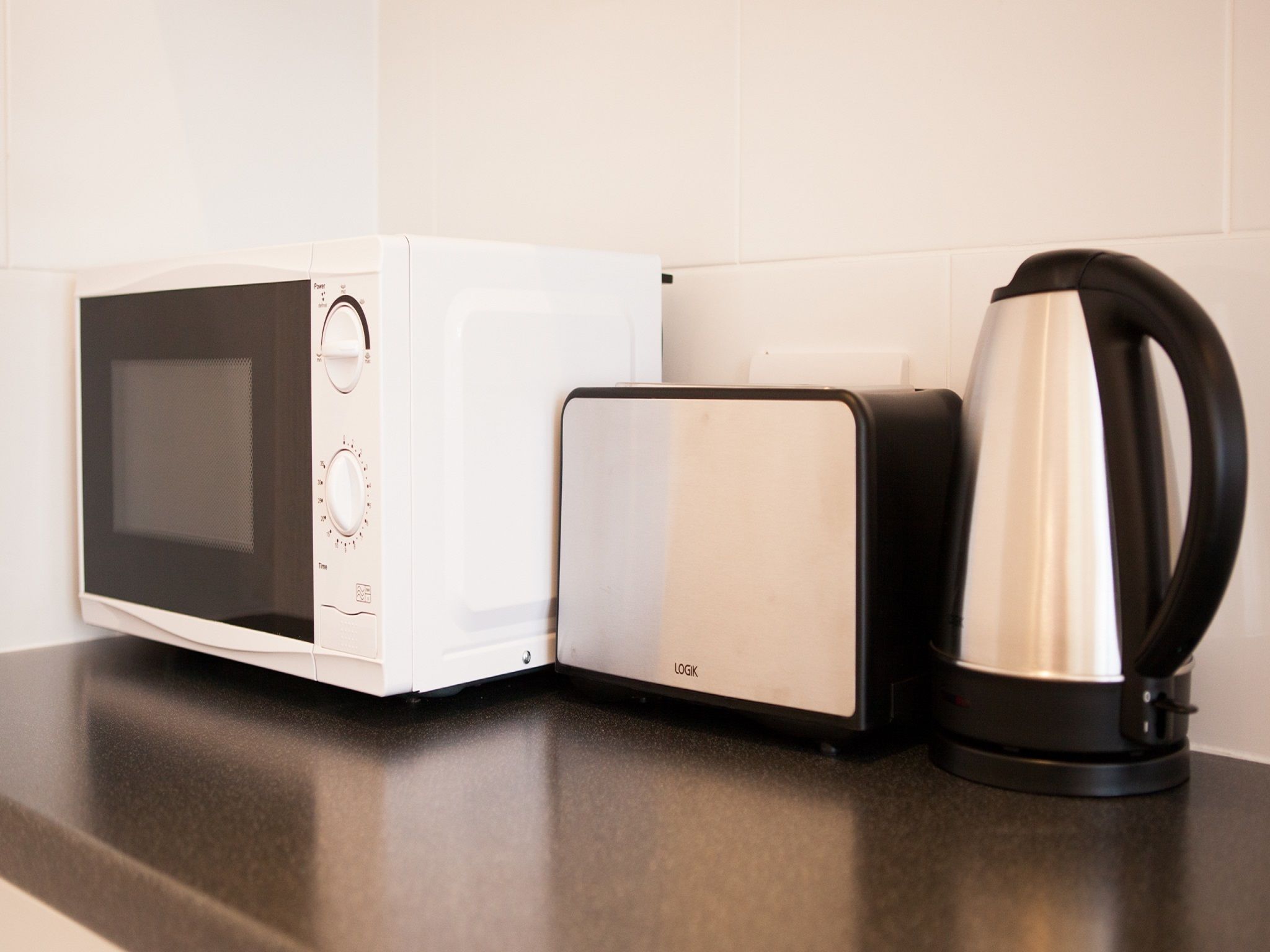 Une cuisine équipée d’un four à micro-ondes, d’un grille-pain et d’une bouilloire, le tout posé sur un plan de travail.