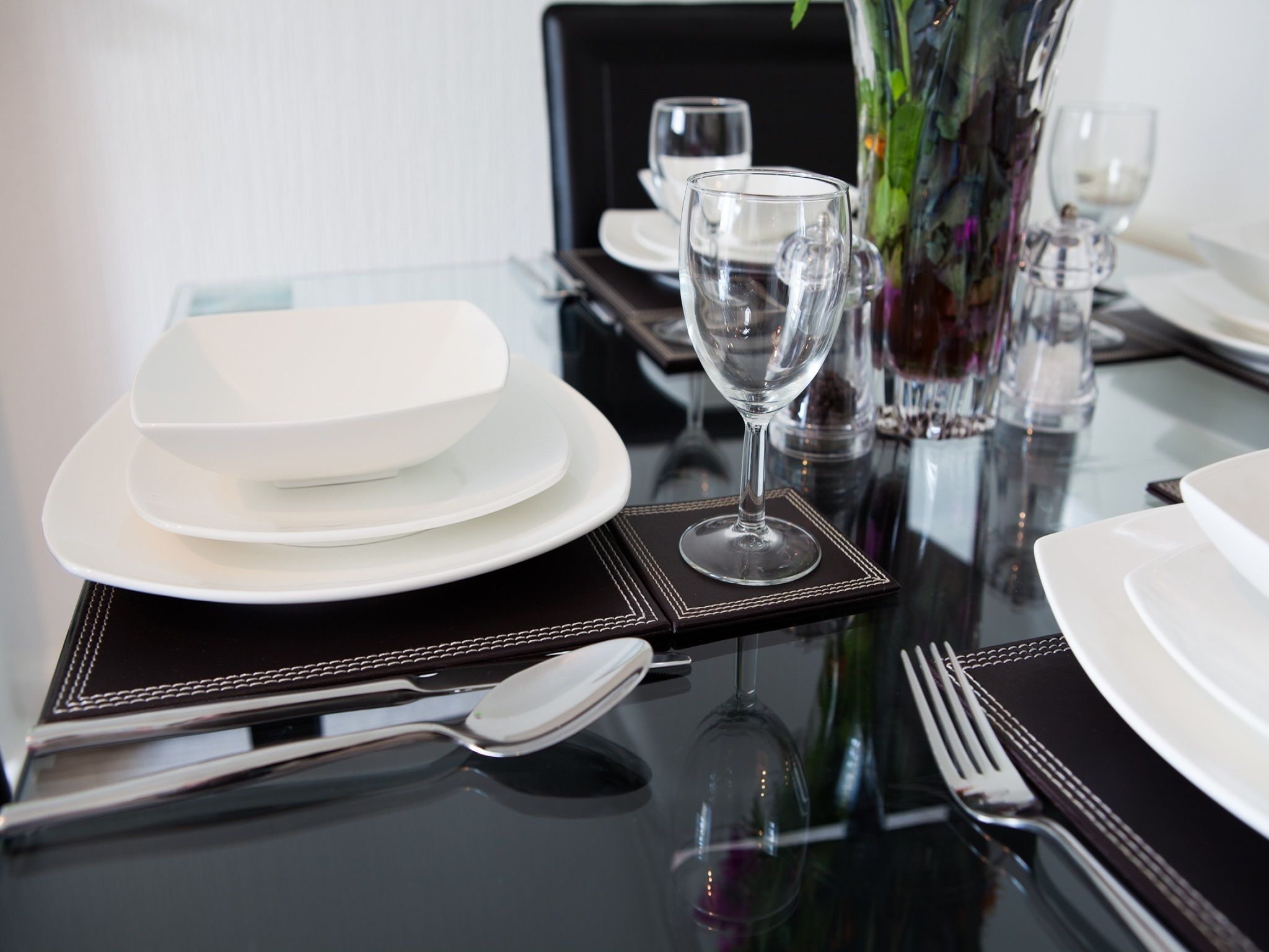 A dining table set with white plates, bowls, wine glasses, and cutlery.