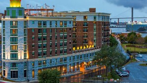 A multi-story hotel with a prominent tower featuring a colorful spire, a well-lit facade, and a view of a bridge in the background.