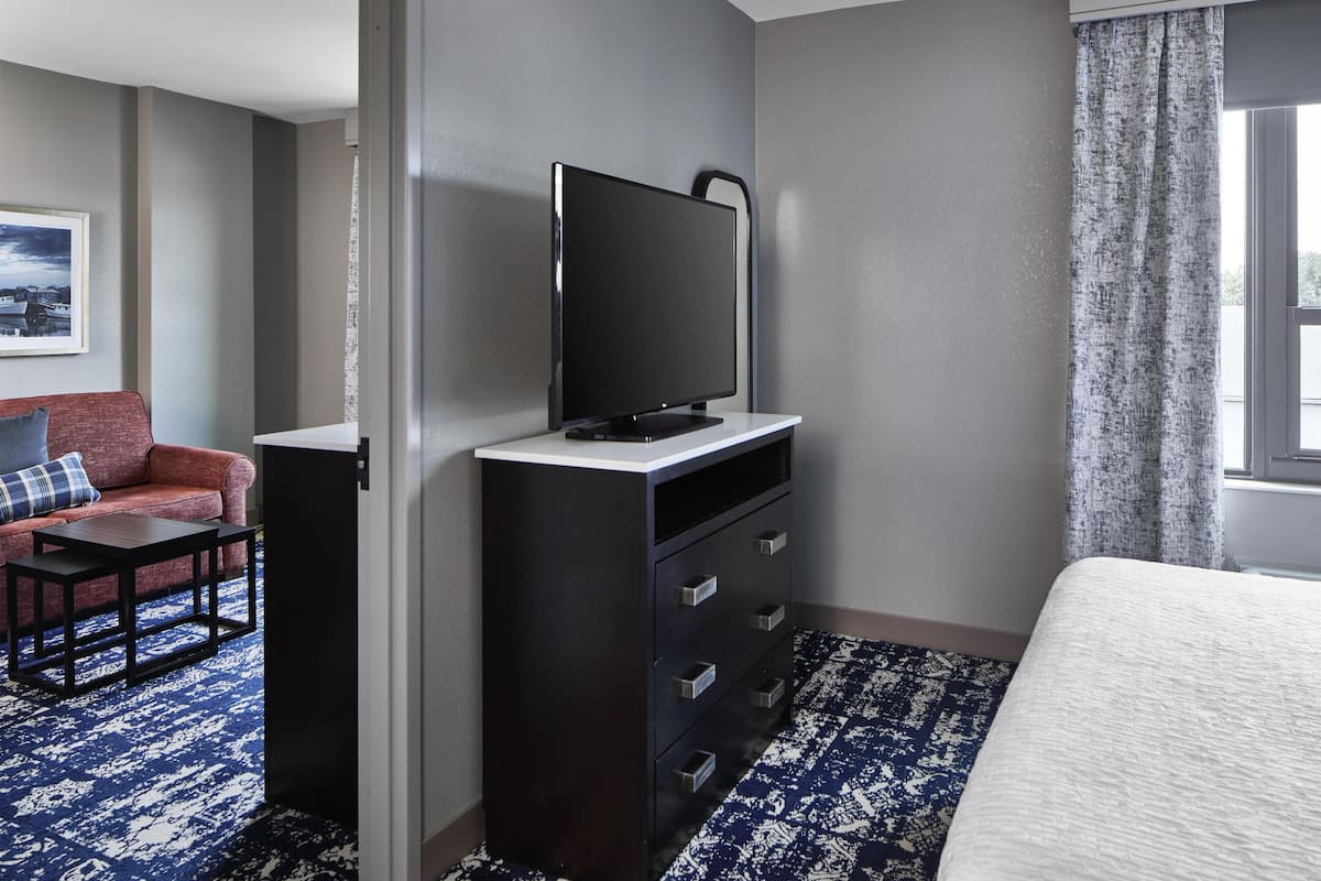 Een hotelkamer met een bed, een televisie op een standaard, een bank, een kleine tafel en een kamerbreed tapijt met een patroon.