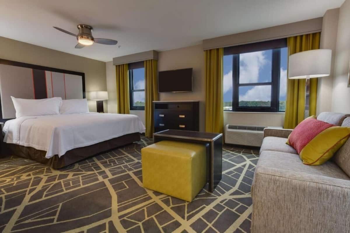 Een hotelkamer met een bed, een slaapbank, een televisie, een bureau en een raam met gordijnen.