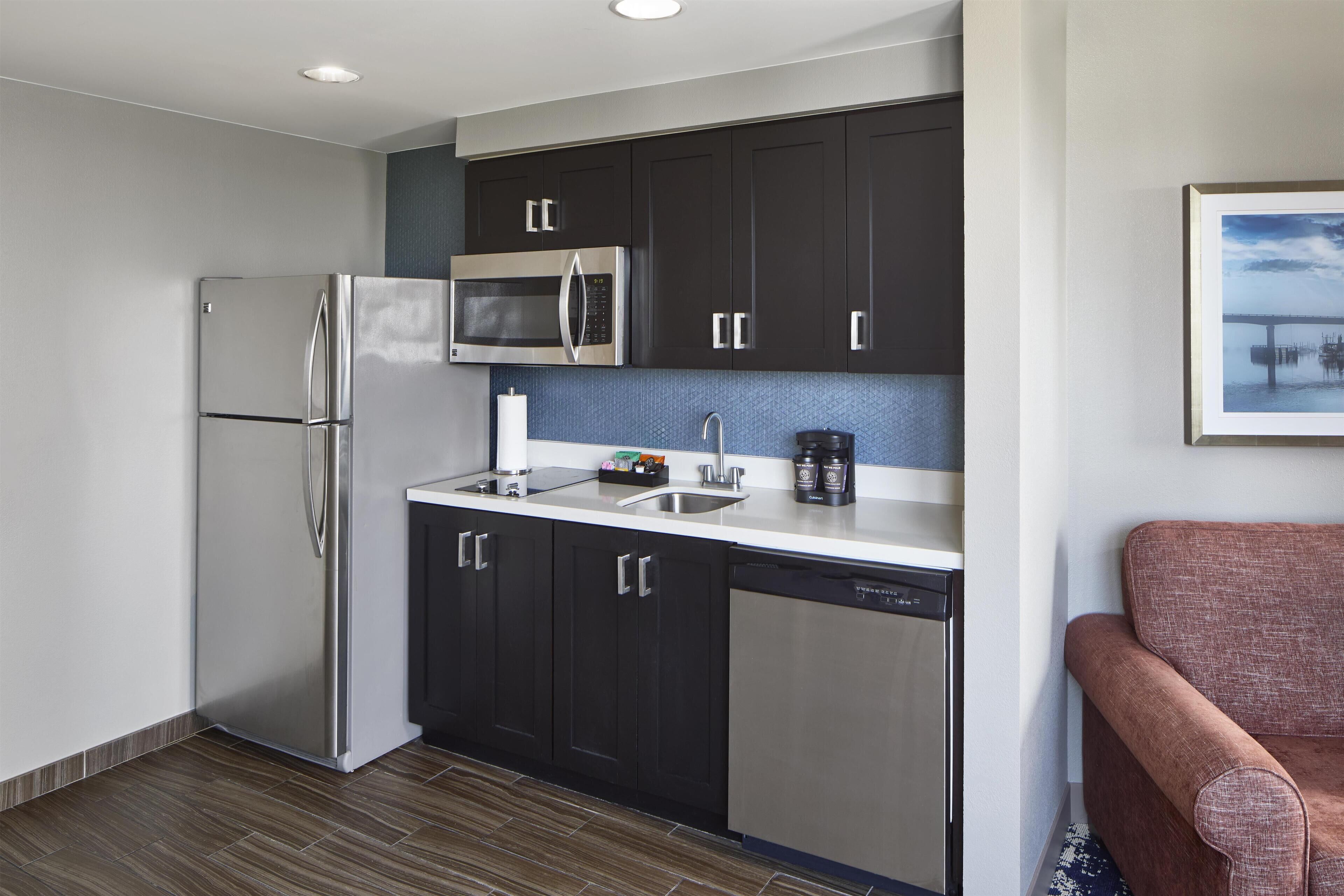 A modern kitchen with dark cabinets, stainless steel appliances, and a dishwasher.