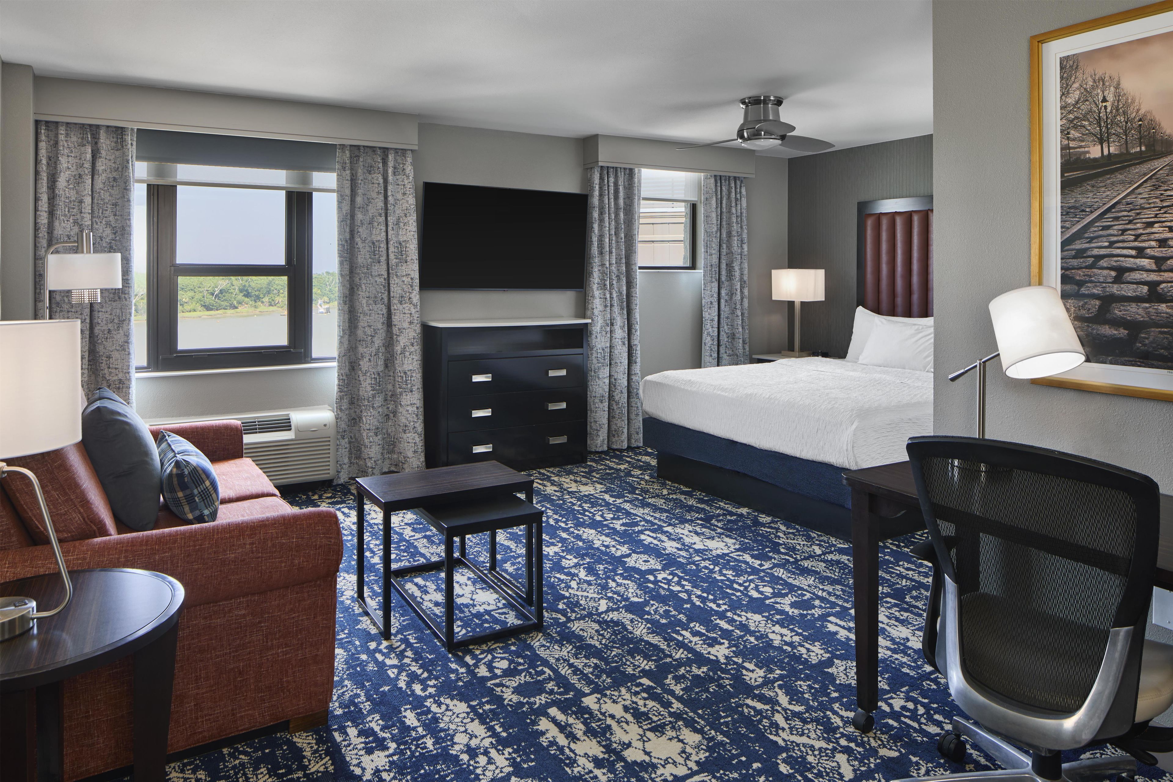 A hotel room with a bed, a desk, a chair, a TV, and a window with curtains.