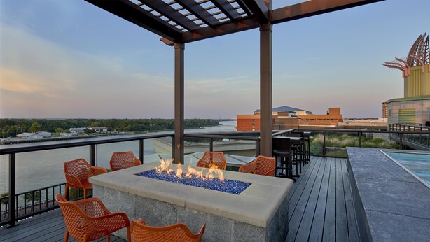 A deck with a fire feature, outdoor seating, and a view of a river and buildings.