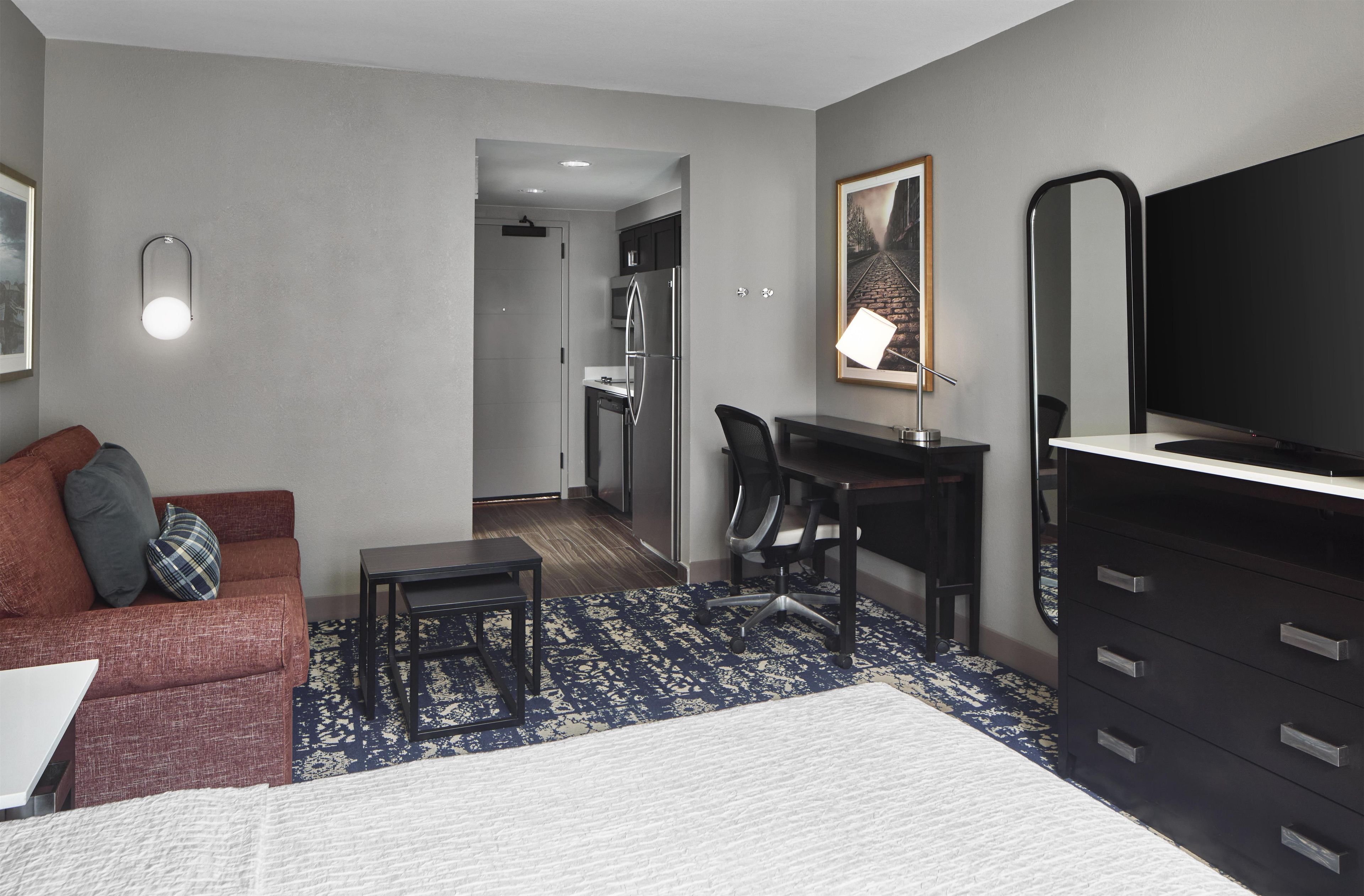 Une chambre d’hôtel avec un lit, un bureau, une chaise, une commode, un téléviseur et un tableau au mur.