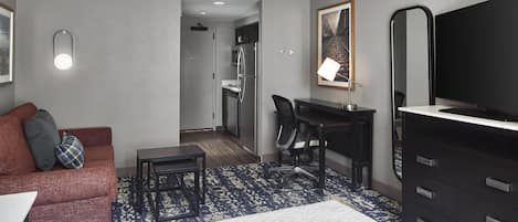 Une chambre d’hôtel avec un lit, un bureau, une chaise, une commode, un téléviseur et un tableau au mur.