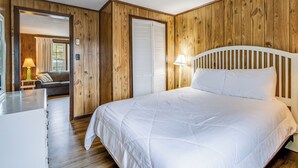 A bedroom with a wooden paneled wall, a white bed with a headboard, a bedside table with a lamp, and a door leading to another room. - The Inn at Lewes (Lewes)
