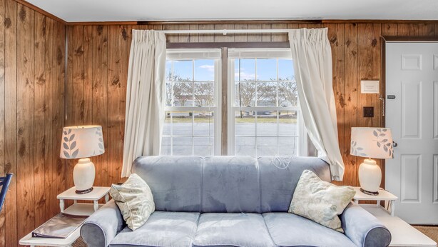 A room with a blue sofa, two bedside tables with lamps, a wooden paneled wall, a door, and a window with curtains. - The Inn at Lewes (Lewes)