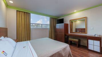 A hotel room with a bed, a desk, a mirror, and a window with curtains.