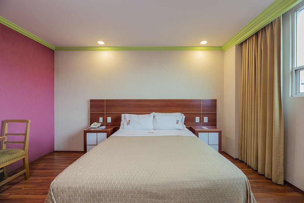 A hotel room with a large bed, two bedside tables, a chair, and a window with curtains.