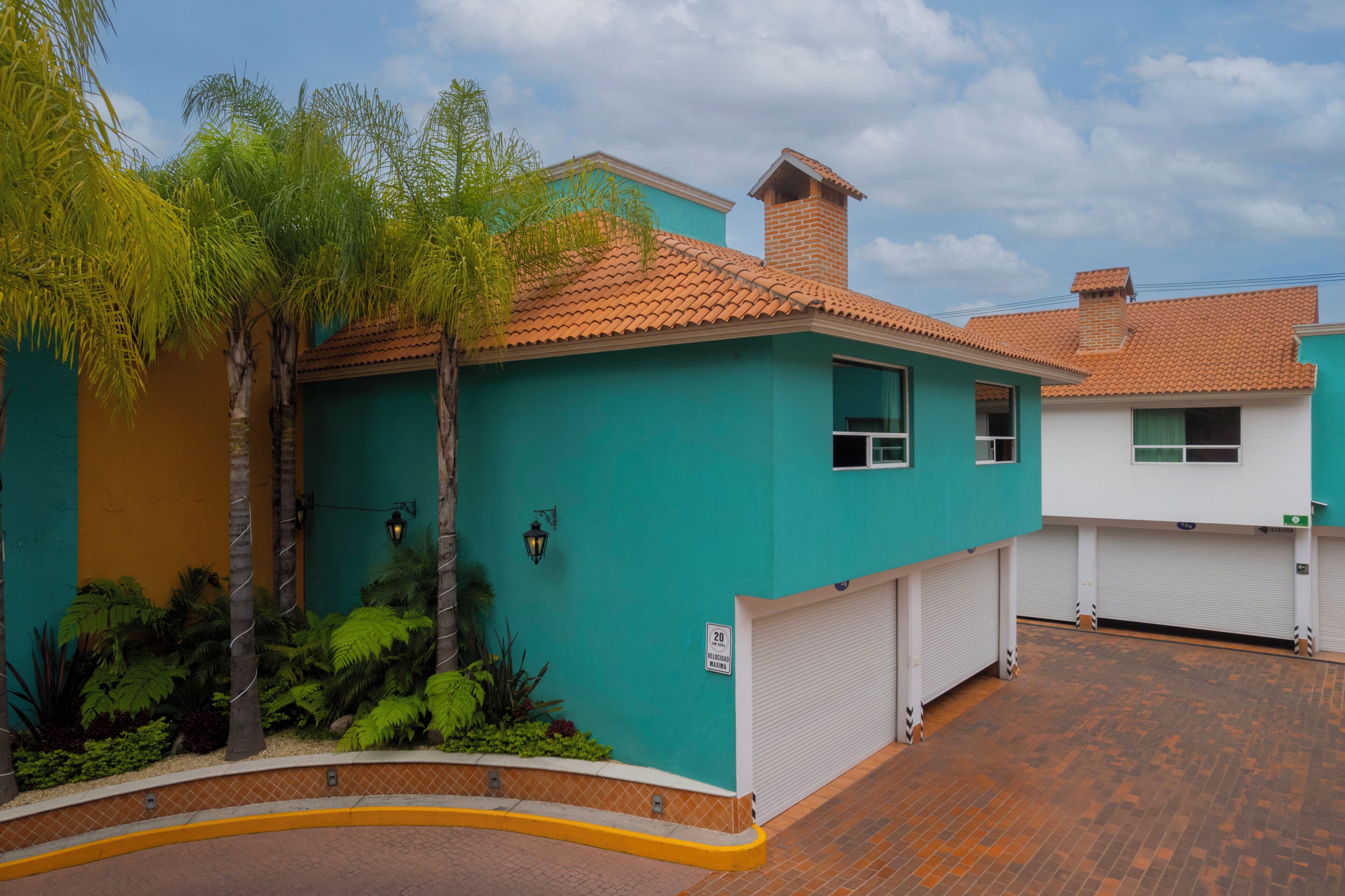 Un edificio residencial con fachada verde, tejado de tejas y entrada con valla.