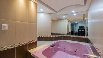 Un bagno moderno con una grande vasca idromassaggio rosa, rivestito in legno e uno specchio che riflette l'ambiente.