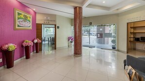 A hotel lobby with a reception desk, a restaurant sign, a large pillar, and a seating area with a view of the street. - Hotel & Villas Panamá (Mexico City)