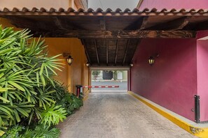 Uma passagem que leva a um portão com telhado de azulejos, cercada por vegetação exuberante.
