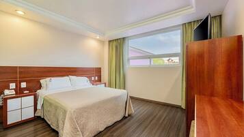 Una habitación de hotel con cama, mesita de noche y ventana con cortinas.