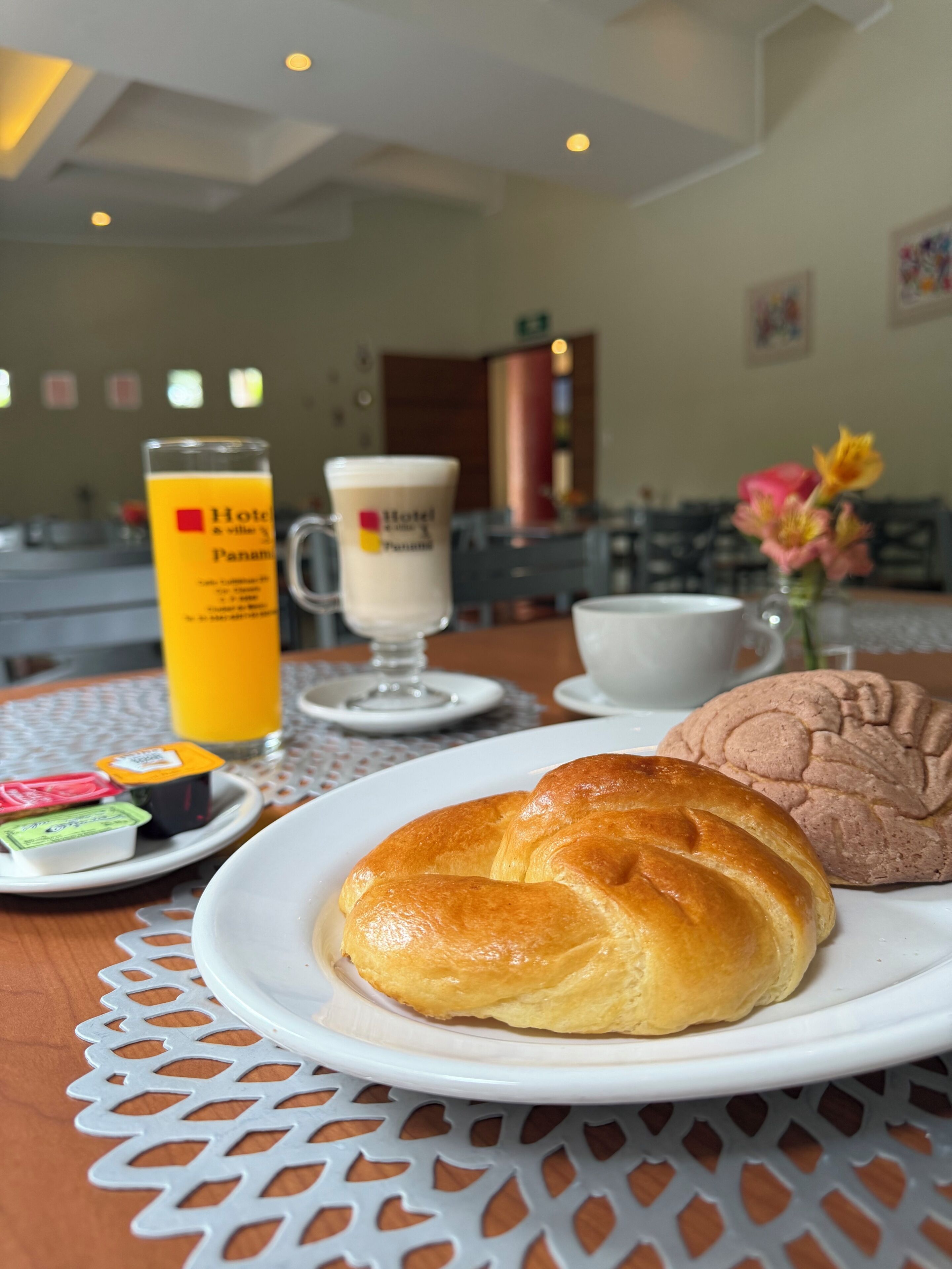 A breakfast setting with a croissant, a muffin, a glass of orange juice, and a coffee cup on a table.