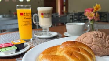 A breakfast setting with a croissant, a muffin, a glass of orange juice, and a coffee cup on a table.