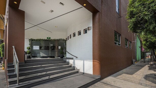 A staircase leading to a building entrance with a metal railing, a green wall with plants, and a clear sky. - Hotel & Villas Panamá (Mexico City)