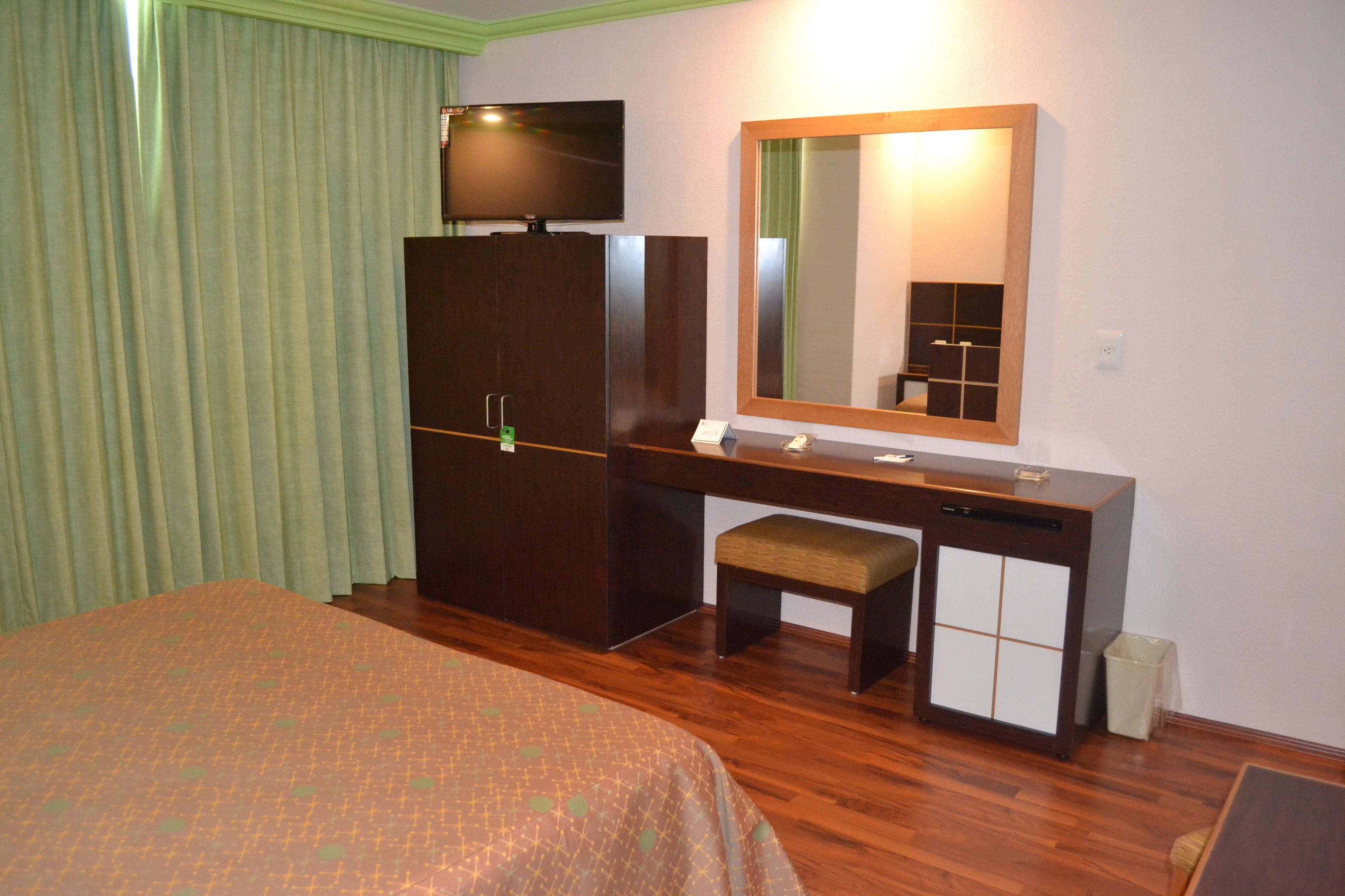 Hotelkamer met een bed, een bureau met stoel, een televisie, een spiegel en een kleine prullenbak.