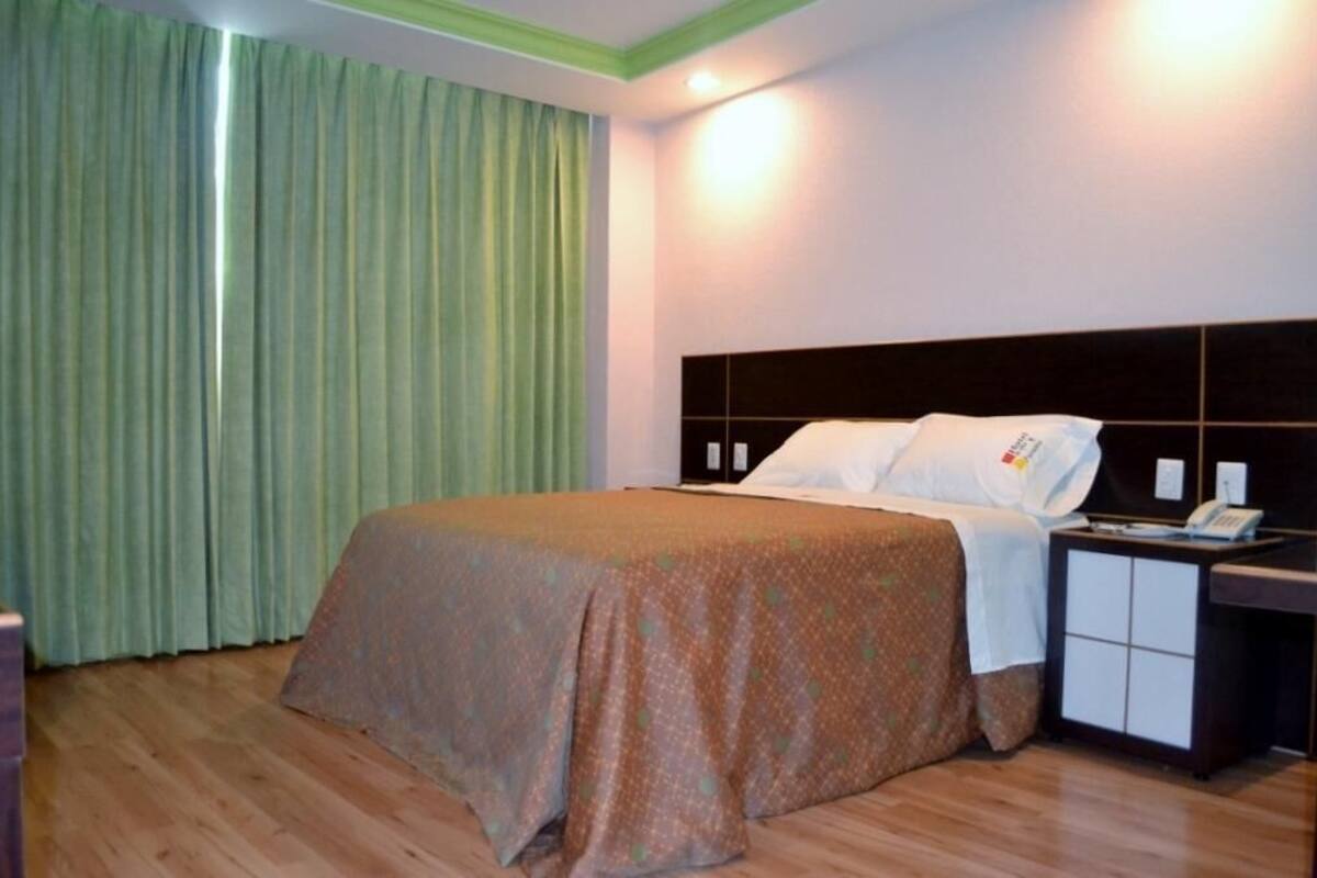 A hotel room with a bed, a nightstand, a telephone, and a green curtain.