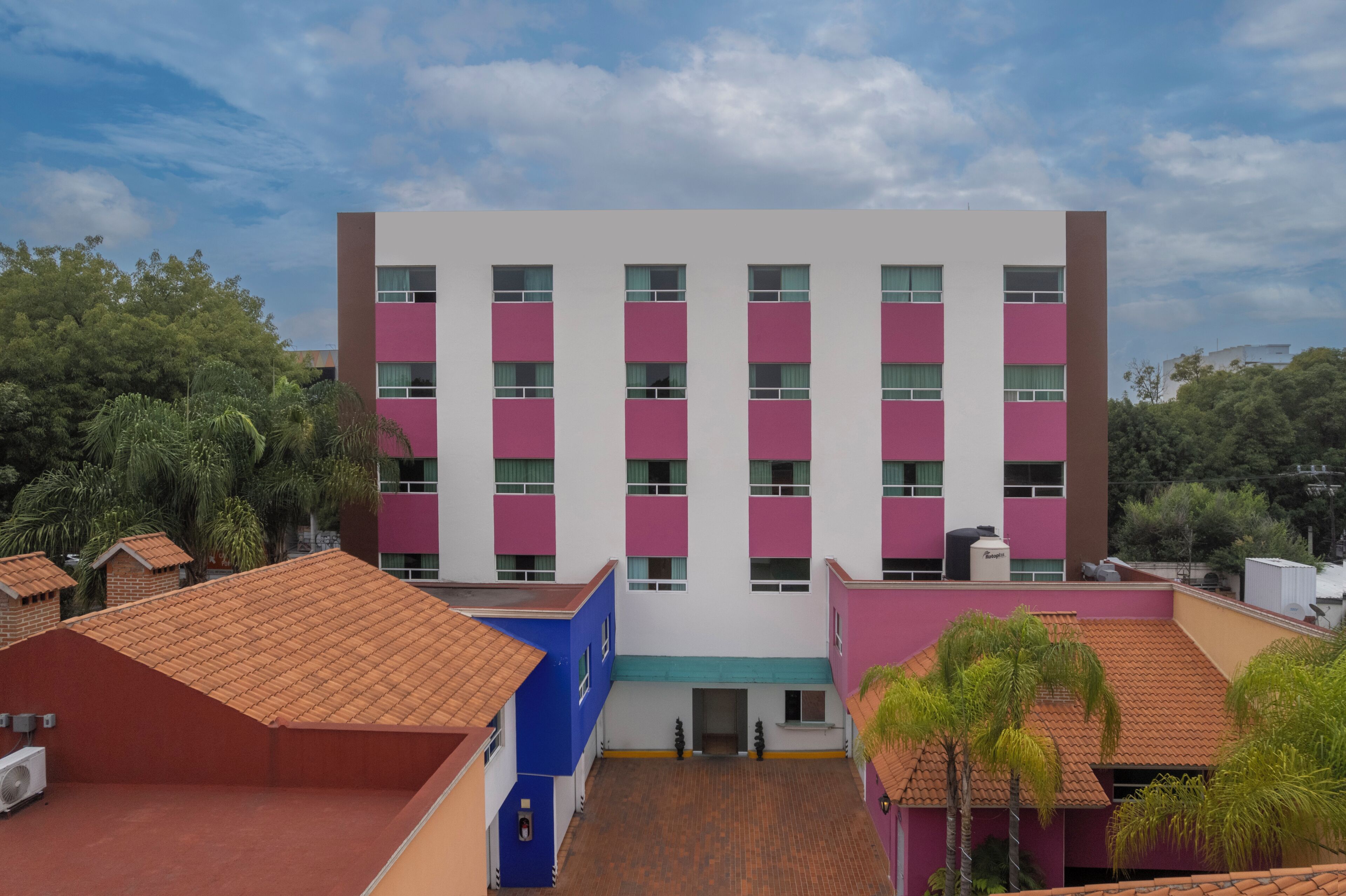 A multi-story building with a central entrance, surrounded by trees and other buildings.