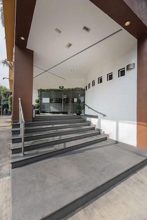 A set of concrete steps leading to a building entrance with a glass door, a metal handrail, and a small sign above the door. - Hotel & Villas Panamá (Mexico City)