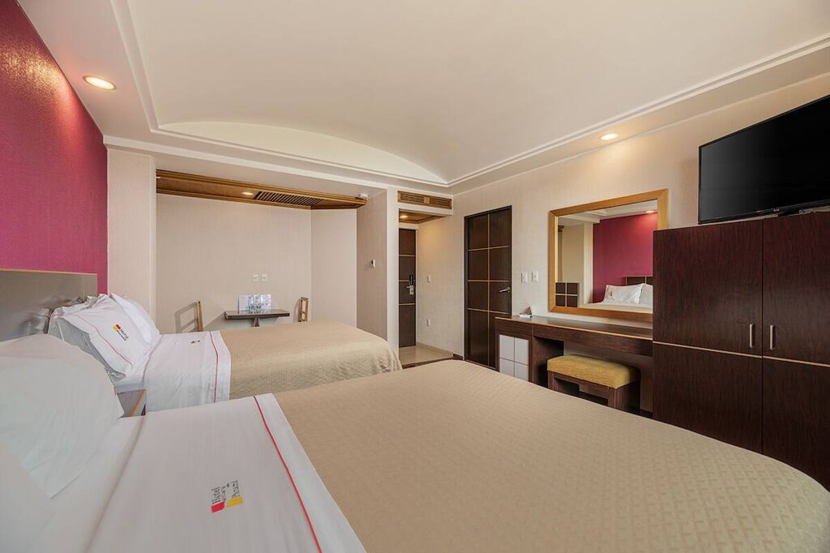 A hotel room with two beds, a desk, a mirror, and a TV.