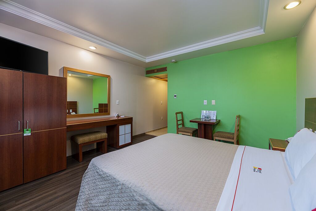 A hotel room with a bed, a desk, a chair, a wardrobe, and a mirror.