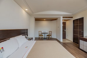 Quarto de hotel com uma cama grande, uma escrivaninha com duas cadeiras, uma mesinha e um guarda-roupa.