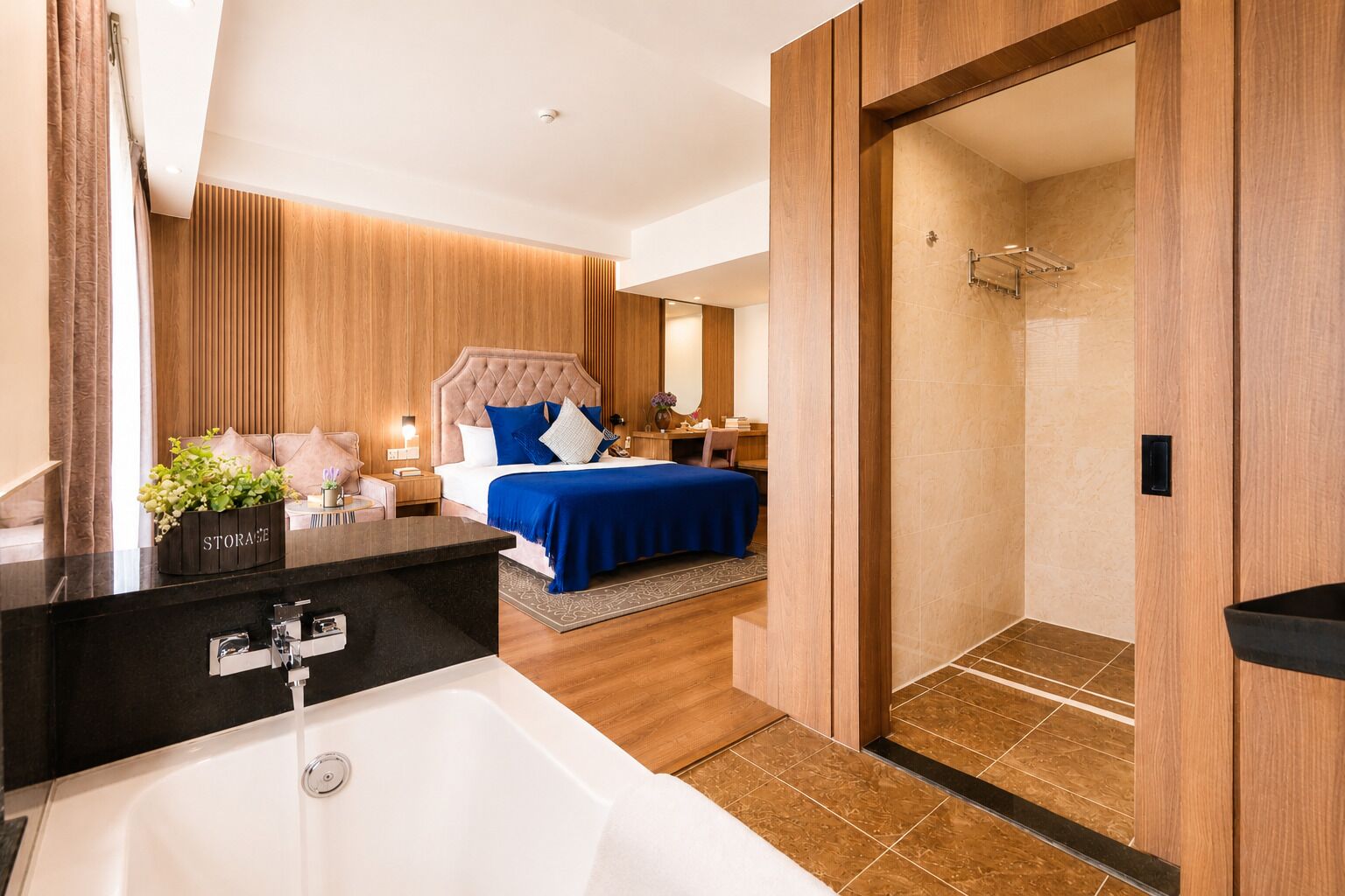 Habitación de hotel moderna con una bañera grande, zona de ducha independiente, cama con ropa de cama azul y pared de paneles de madera.